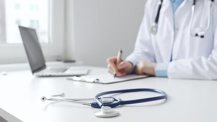 Closeup of blue stethoscope is lying on the table near female doctor professional writing on the clipboard in clinic office. Medicine and healthcare concept - Powered by Adobe