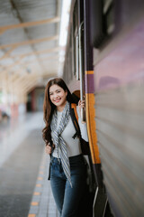 Young female traveler with small backpack at train station. 30s woman waiting for train. Travel. Solo leisure. Back view. No face.