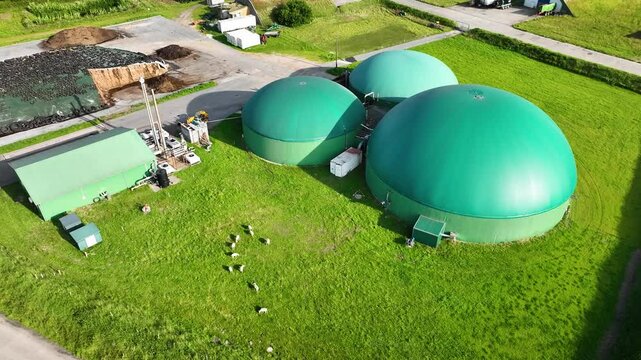 Aerial footage of green-roofed biogas digester facility, combined heat and power station featuring gas pipelines, technical units, silage storage. Sustainable energy production in modern agriculture.
