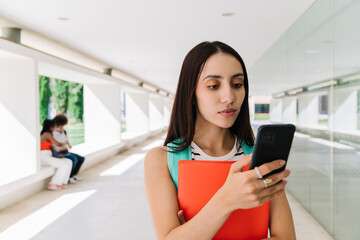 University student using smartphone in corridor with books and backpack