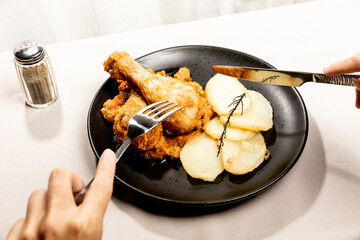 Hands cutting chicken with vegetable sauce and potatoes served on a black dish