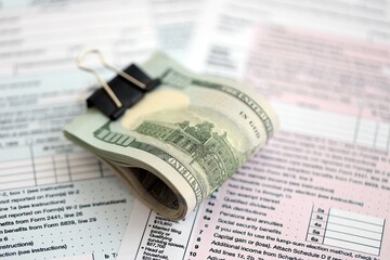 Big amount of United States hundred dollar bills on table with individual income tax return form...