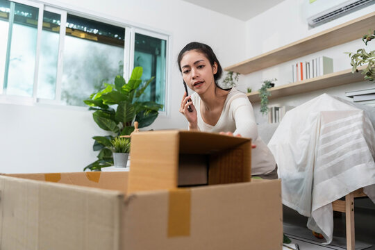 Moving process. Young woman packing boxes while on a phone call in a cozy home environment.