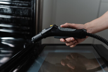 Housekeeper male cleaning oven with steam cleaner in modern kitchen, holding steam cleaner gun while effectively removing grease and ensuring hygienic cooking environment, close-up.