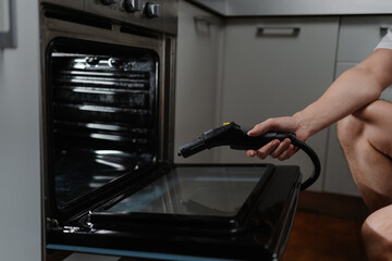 Side view cropped shot of unrecognizable housekeeper steam cleaning kitchen oven surface, targeting stubborn grease with powerful cleaning equipment for spotless, sanitized cooking space, close-up.