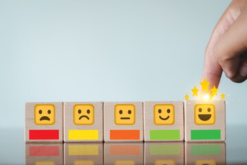 Hand adding gold stars to a happy face emoji block in a customer satisfaction rating scale over...
