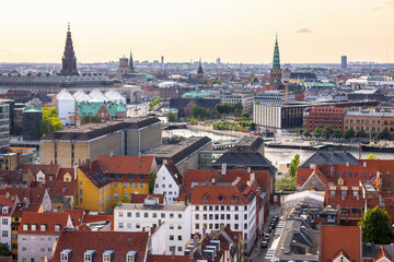 Panoramic view of Copenhagen taken from the top of the Church of Our Saviour, showing a mix of historical rooftops, modern buildings, and city landmarks under a warm evening sky.