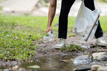 Nature Conservation Efforts. A volunteer picking up plastic bottles near a stream.