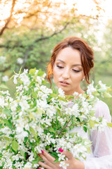 Naklejka premium A young woman with red hair, in a white dress, holds a bouquet of white flowers. Her gaze is directed downwards, creating an atmosphere of tenderness and thoughtfulness.