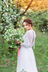 Young woman in white dress with transparent cape holding bouquet of white flowers standing in...