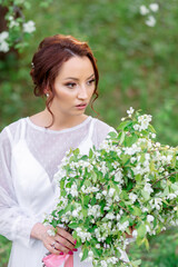 A young woman with red hair in a white dress holds a bouquet of white flowers, surrounded by...