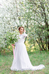 A gentle girl in a white dress with a bouquet of flowers against the background of blooming trees,...