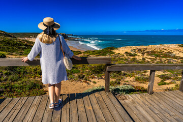Mature woman in summer hat tourist standing at viewpoint to Monte Clerigo beach on Algarve coast on...