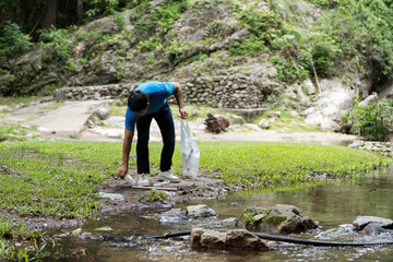 Volunteer Picking Up Waste. A young man collects plastic from a stream during a clean-up event.