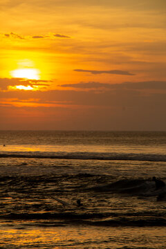 Sunset over the ocean with surfers in silhouette
