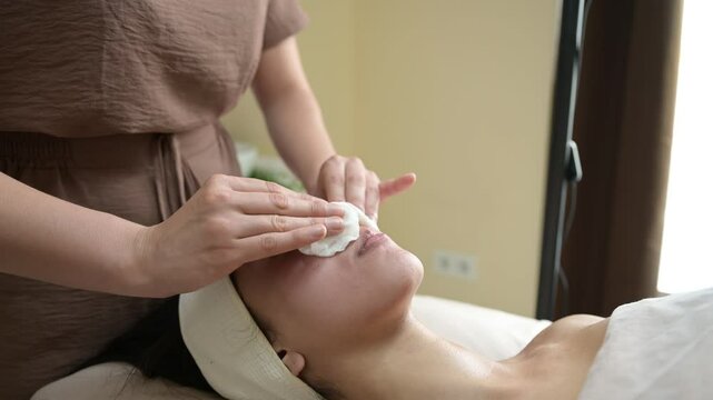 Beautician applying lotion on woman's face with cotton pads