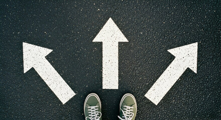 Overhead view of three white arrows on dark asphalt, pointing different directions, with feet in the center