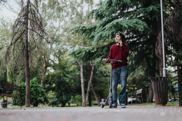 Obraz premium A man stands in a park, talking on his phone while holding an electric scooter. The scene conveys a sense of relaxation and modern urban lifestyle amidst lush greenery.