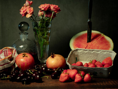 Still life with rose flowers, summer fruits, bottles of wine and a glass of wine. Pomegranate, cherry, sweet cherry, strawberry and watermelon. Alcohol. The still life is stylized as an old painting.