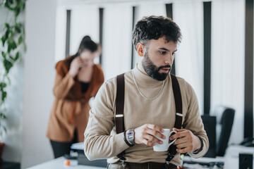 A focused individual holding a coffee cup in a contemporary office, with a blurred colleague...