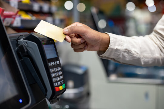 A hand holding a credit card over a payment terminal during a purchase in a store. Contactless payment concept.