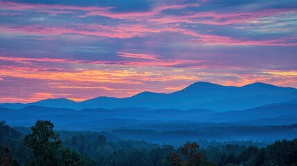 Obraz premium Colorful sunrise over blue mountain ranges with vibrant clouds and misty forests in the foreground