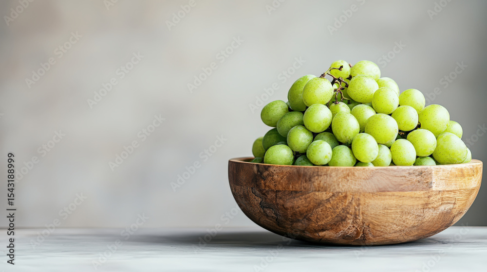 Poster wooden bowl filled with fresh green grapes sits on light surface, creating simple and natural aesthe