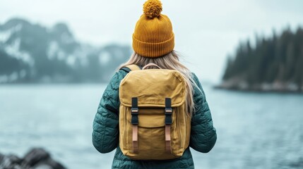 A traveler with a bright yellow backpack gazes at a serene lake, surrounded by mountains, embracing nature's beauty and the essence of adventure and exploration.