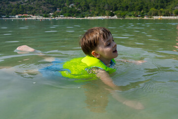 Small child swimming in life jacket in shallow water. Summer recreation. Safety of child while...