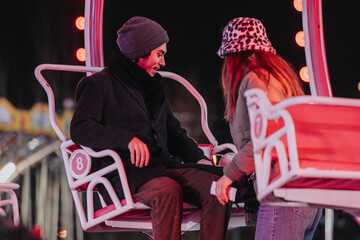 A young couple shares a joyful and intimate moment on a Ferris wheel during an evening visit to an...