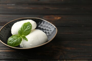 Pieces of delicious mozzarella cheese and basil in bowl on wooden table, closeup. Space for text