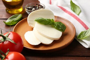 Tasty mozzarella, tomatoes and basil on wooden table, closeup