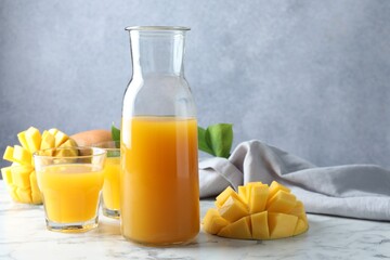 Tasty mango juice, fresh fruits and green leaves on white marble table