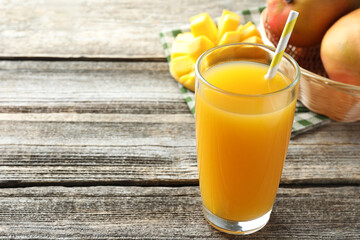 Tasty mango juice in glass and fresh fruits on wooden table, closeup. Space for text
