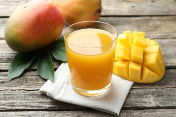 Tasty mango juice in glass, fresh fruits and green leaves on wooden table, closeup