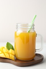 Tasty mango juice in glass mason jar, fresh fruit and mint on white table, closeup