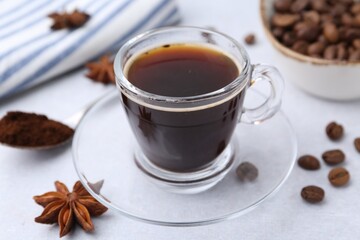 Cup of aromatic coffee, beans and star anise on white table, closeup