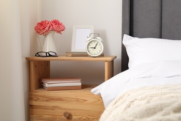 Bedside table with alarm clock, flowers and decor near bed indoors