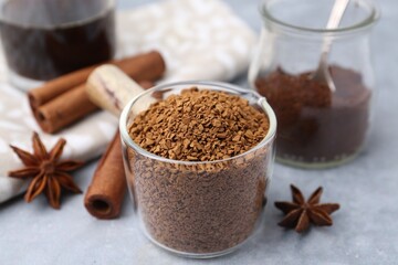 Granulated instant coffee in measuring cup and spices on grey table, closeup