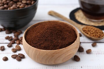 Instant coffee powder in bowl and beans on white wooden table, closeup