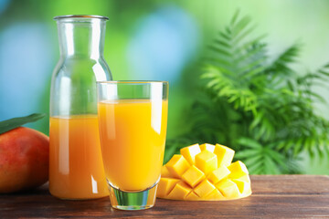 Tasty mango juice in glass, carafe and fresh fruits on wooden table against blurred background,...