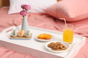 Tray with delicious breakfast and flowers on bed indoors, closeup