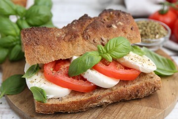 Tasty sandwich with mozzarella cheese, tomatoes and basil on white wooden table, closeup