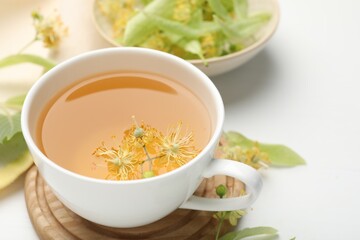 Fresh linden tea in cup and flowers on white table, closeup