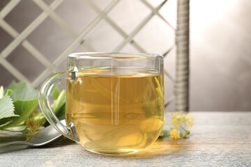 Fresh linden tea in cup and flowers on wooden table, closeup