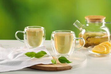 Tasty green tea in glass cups, teapot, lemon and leaves on white table outdoors, closeup