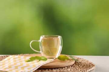 Tasty green tea in glass cup and leaves on white marble table outdoors