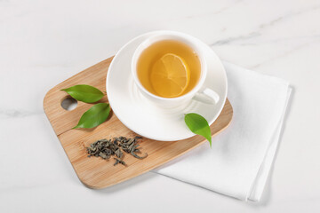 Tasty green tea with lemon in cup, brew and leaves on white marble table, above view