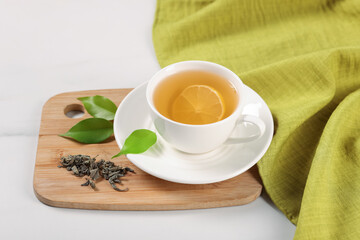 Tasty green tea with lemon in cup, brew and leaves on white marble table, above view