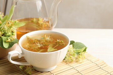 Fresh linden tea in cup, teapot and flowers on white table, closeup. Space for text